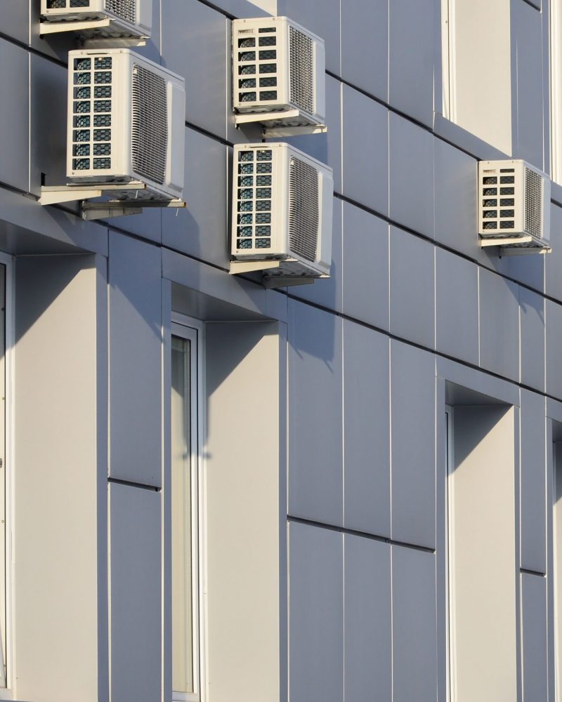 Gray wall of office building made of metal plates with windows and air conditioners